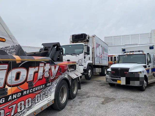 Priority Towing wrecker with commercial trucks at the yard